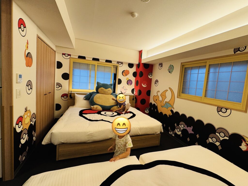 Children playing excitedly with a life-sized Snorlax plush on the bed in a Pokémon-themed hotel room.