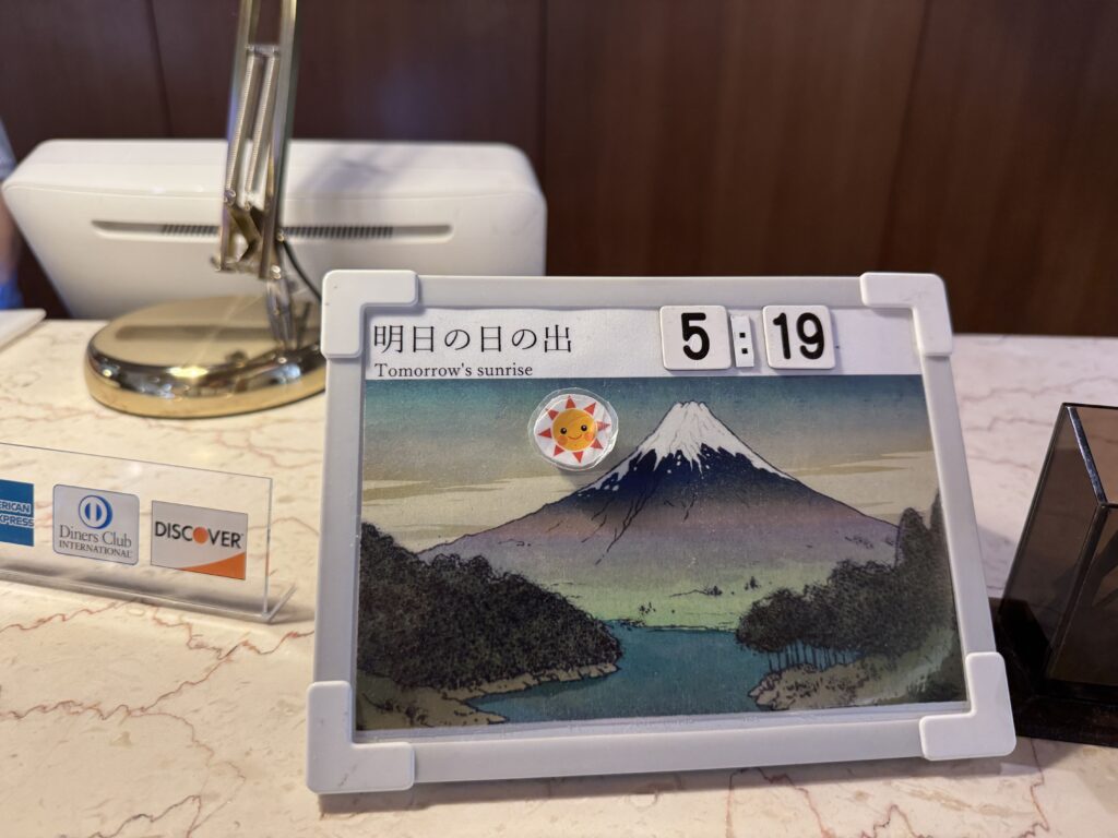 A board at Kyukamura Fuji’s front desk showing the next day’s sunrise time—a helpful tip for sunrise watchers and photographers.