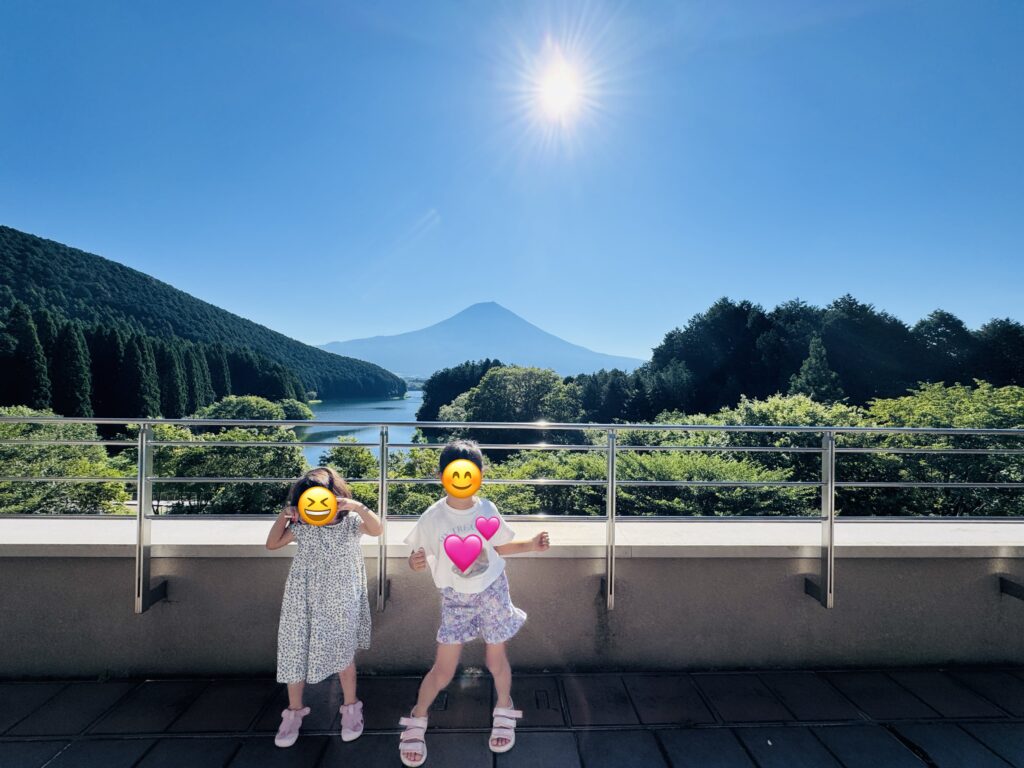 View from the terrace of Kyukamura Fuji at Lake Tanuki on a sunny day, with two daughters posing for a photo.