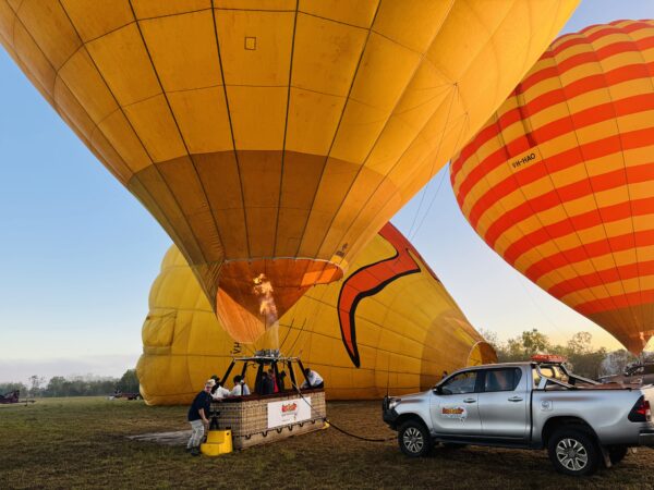 Hot air balloon in Cairns preparing for takeoff, with bright burner flames lighting up the balloon just before liftoff.