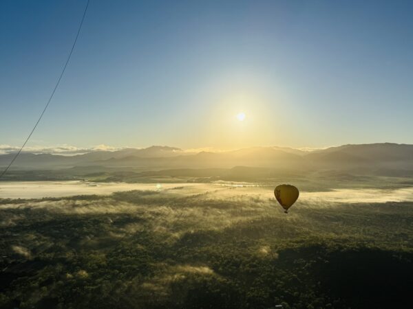 Hot air balloon soaring above the Mareeba Tablelands near Cairns, reaching cloud level with the golden morning light illuminating the landscape below.