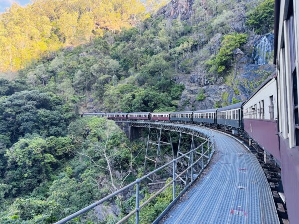 View from the Kuranda Scenic Railway of the sweeping curve at Stoney Creek Falls, with the train stretching along the mountainside through World Heritage rainforest.