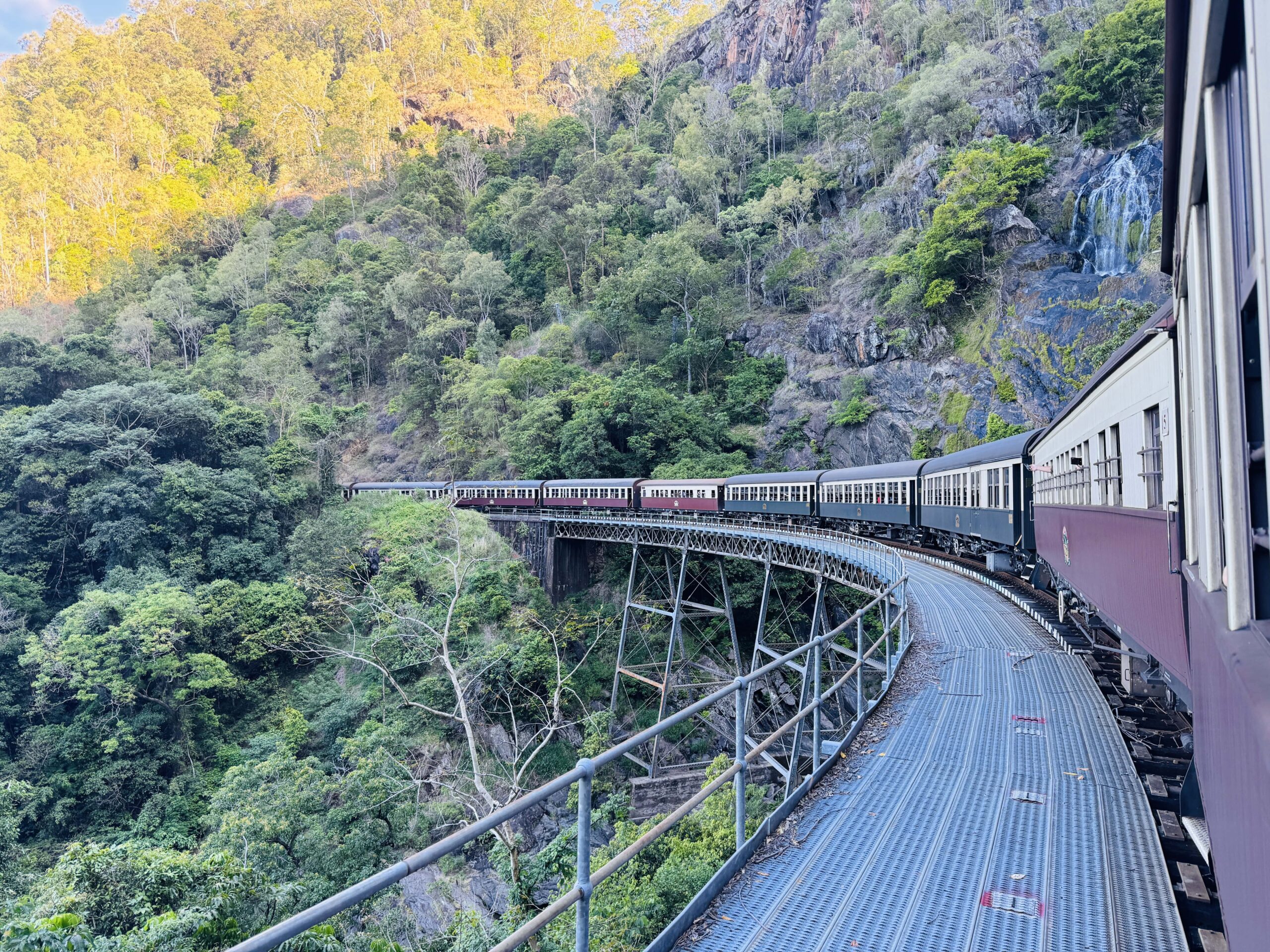 View from the Kuranda Scenic Railway of the sweeping curve at Stoney Creek Falls, with the train stretching along the mountainside through World Heritage rainforest.